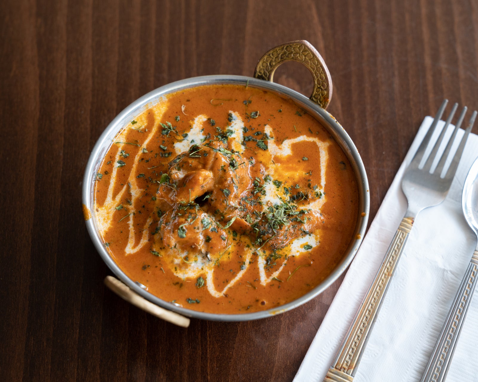 A bowl of butter chicken on a restaurant table with a fork and napkin
